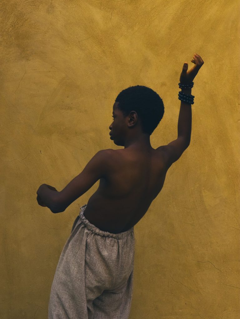 Jeune danseur de dos, bras levé, devant un mur ocre